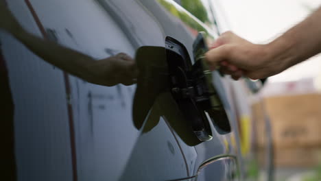 close up of driver opening electric vehicle charging port flap to charge battery