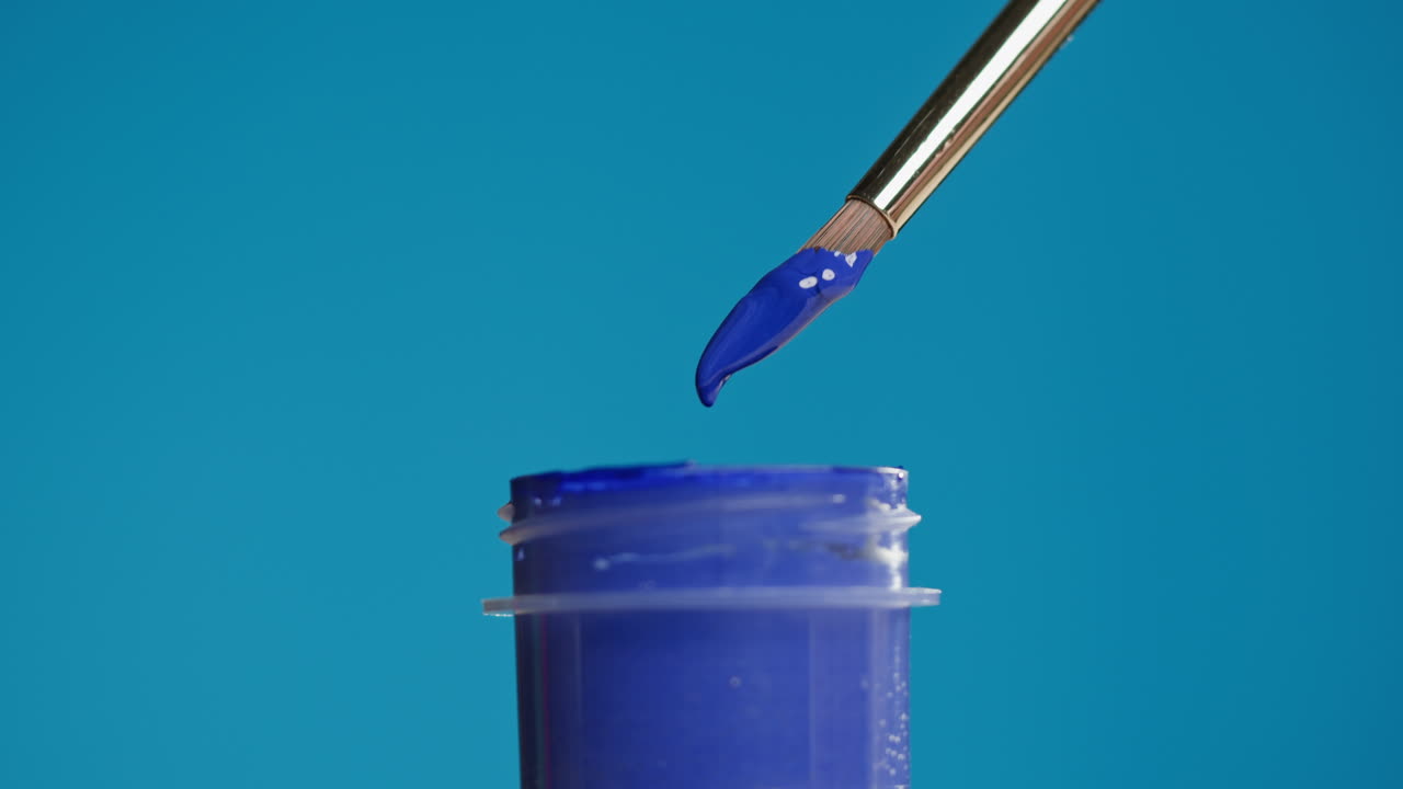 Pinsel taucht in blaue Farbe und lässt einen Tropfen fallen