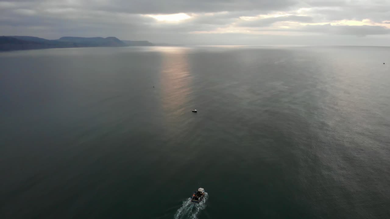 일출 이른 아침 배경에 쥬라기 해안을 배경으로 라임 만을 가로질러 라임 레지스 사우스 웨스트 잉글랜드를 떠나는 어선을 따라 항공 샷