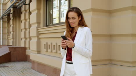 playful business woman texting on mobile phone outdoors. smiling woman