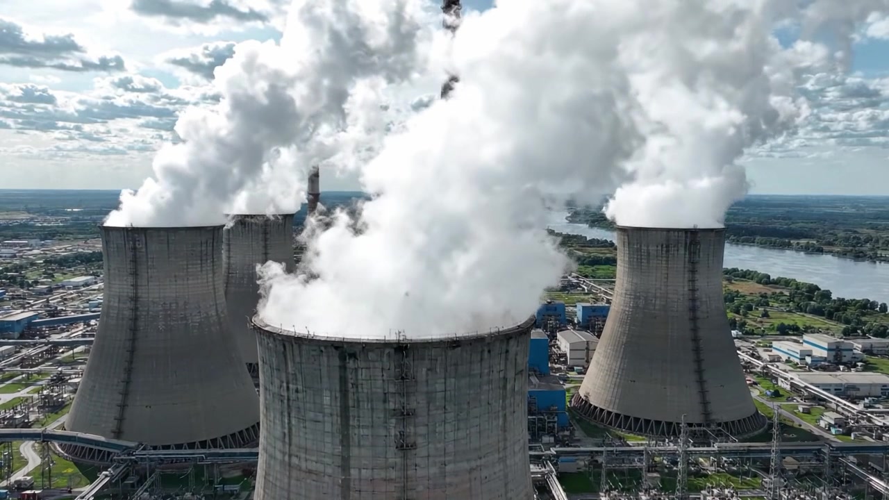Vista Aerea di Torri di Raffreddamento che Emettono Vapore in un Paesaggio di Centrale Elettrica Sotto un Cielo Nuvoloso Drammatico - Focus su Produzione di Energia e Impatto Ambientale.