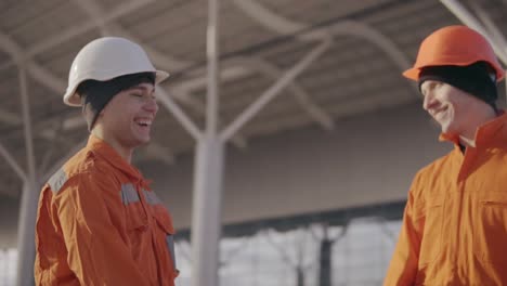 two construction workers high five. they look very happy. new constructed building with columns at the background