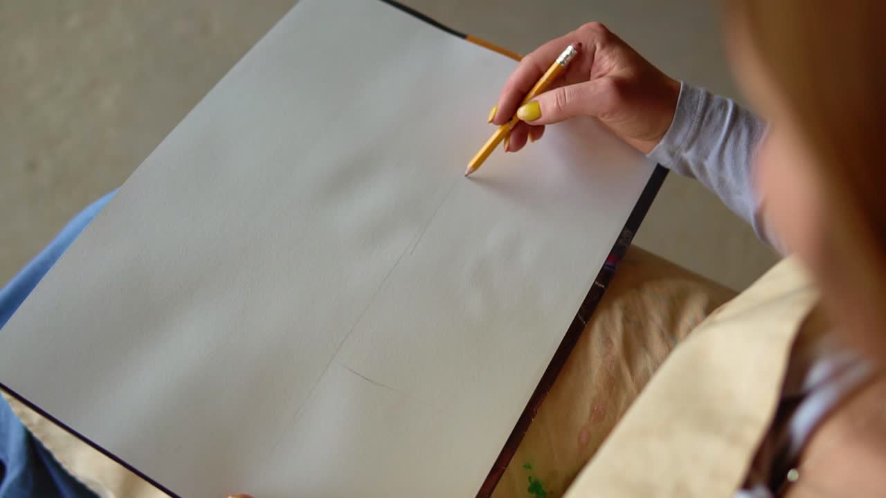 Hand of female with yellow manicure drawing at paper in her studio. Woman's hand draws. Designer clothes or tailor, animator, artist or illustrator. Female artist's hand sketching with a pencil on a light day. High angle view