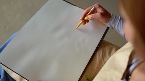 hand of female with yellow manicure drawing at paper in her studio. woman's hand draws. designer clothes or tailor, animator, artist or illustrator. female artist's hand sketching with a pencil on a light day. high angle view