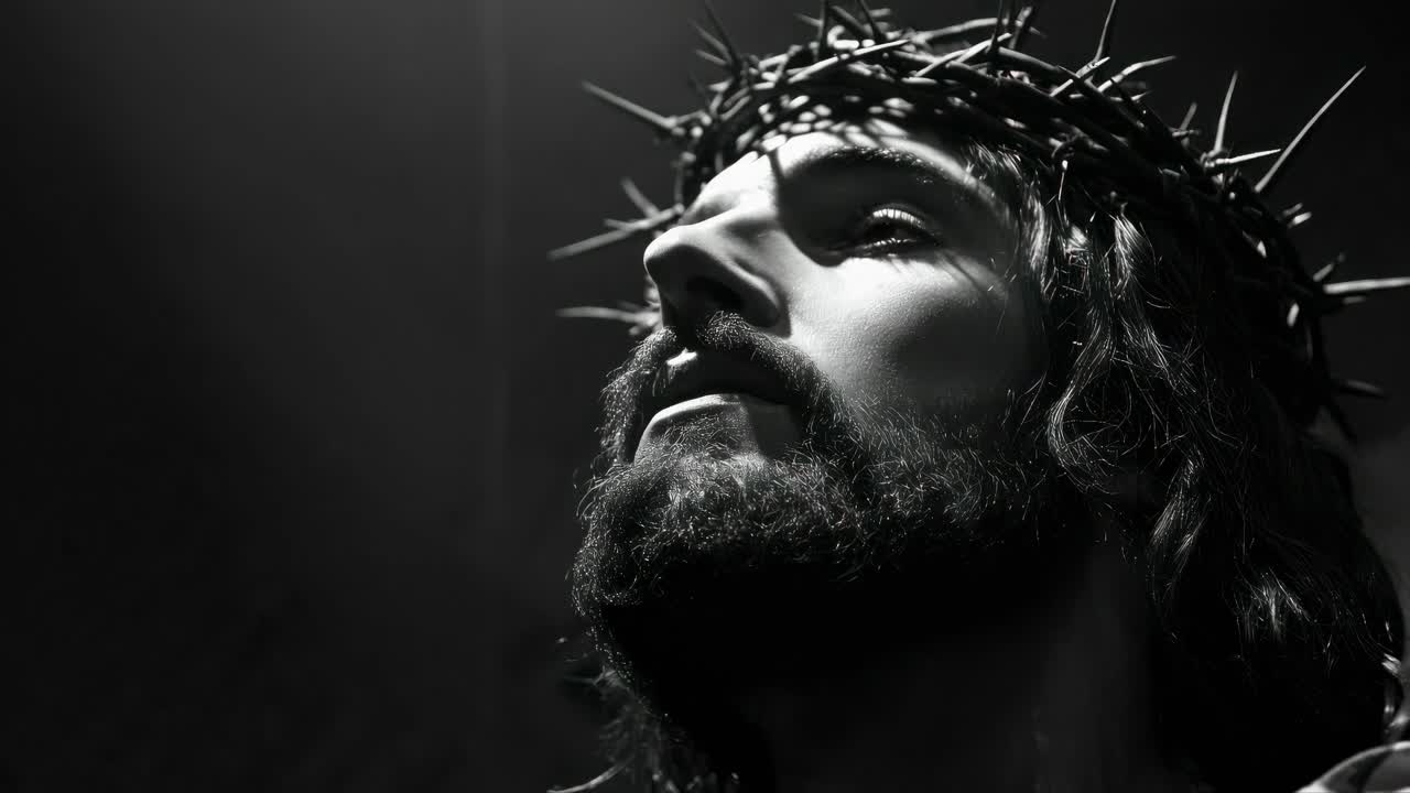 Dramatic black and white video still of a bearded man with a crown of thorns, captured from a low