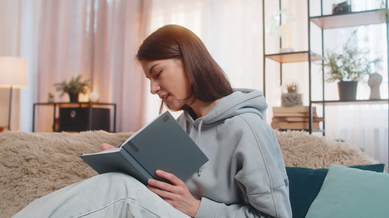 Happy woman planning workday sitting on sofa couch holding pen and notebook looking focused at home