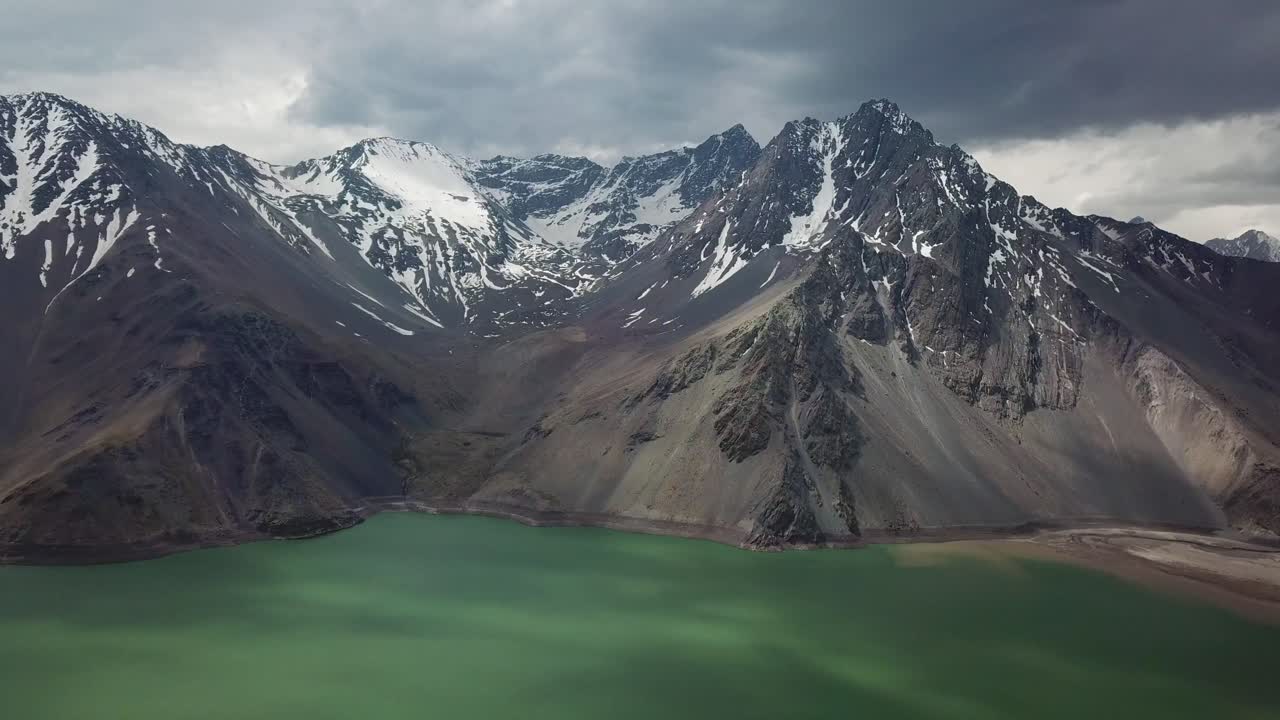 Cinematic Aerial View of Green Lake Under Snow Capped Andes Mountain Peaks, Yeso Dam, Chile