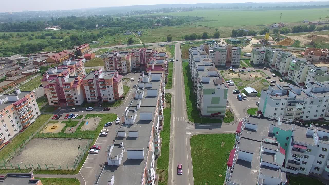 cars are passing along the road of the new district of the city on the background of high-rise buildings near the construction of modern buildings. Aerial view