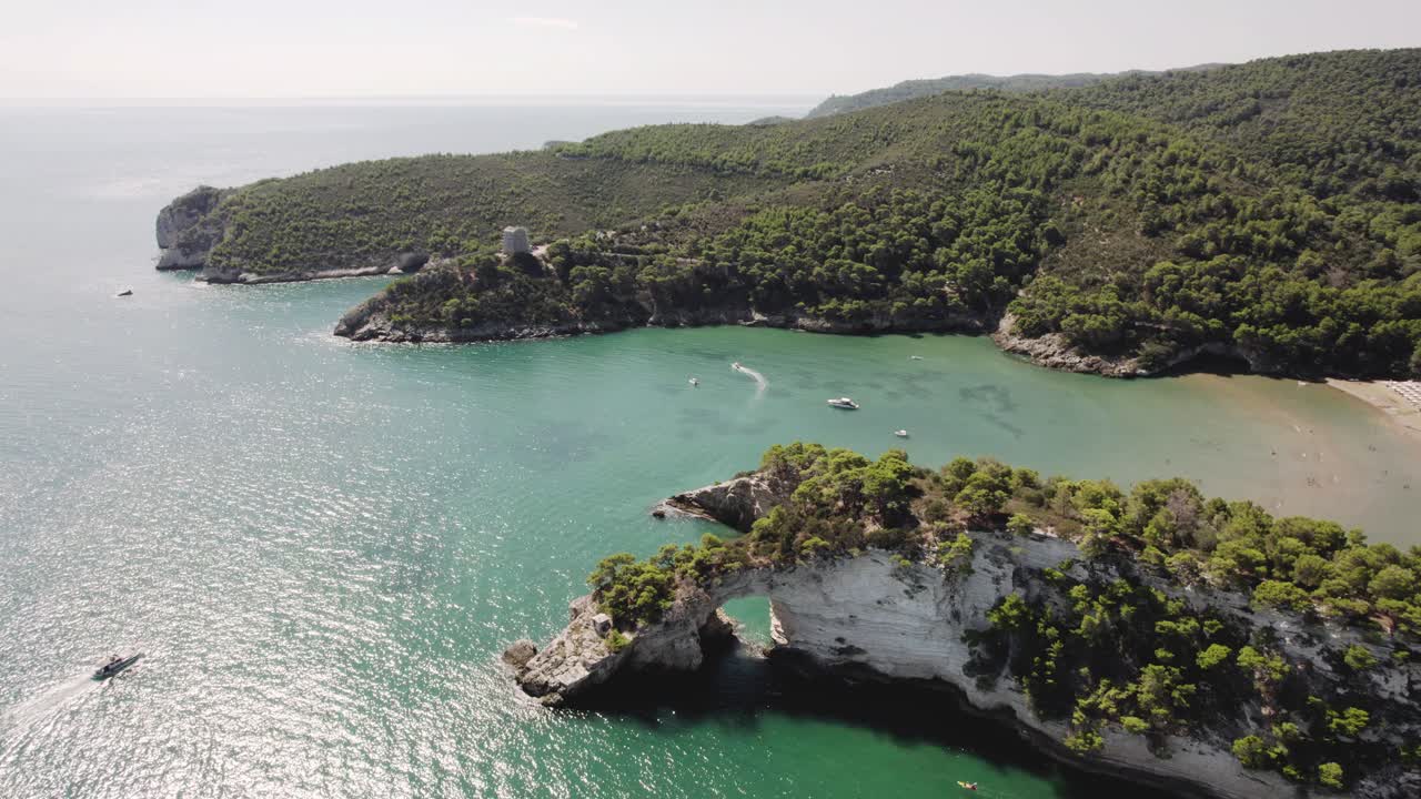 drone volando hacia atrás con la cámara inclinándose lentamente mostrando un arco en el mar en la costa del parque nacional de gargano, italia en 4k