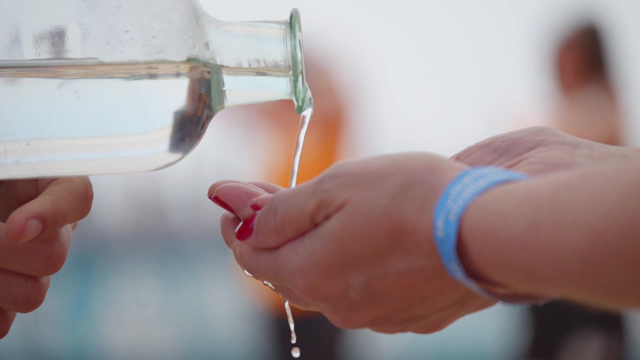 ガラス瓶からすくった手にきれいな水が注がれているクローズアップ。新鮮さ、水分補給、洗浄、そして不可欠な天然資源へのアクセスを表現しています。