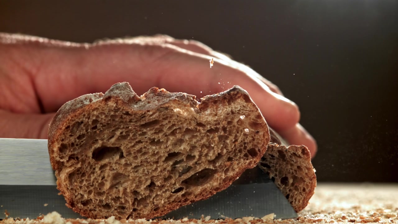 Close-Up of Hand Slicing Rustic Bread with a Knife in Slow Motion