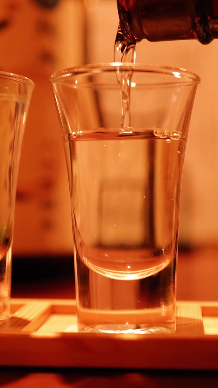 Vino di riso trasparente viene versato in bicchieri di vetro sotto una calda illuminazione ambientale in un bar di Tokyo.