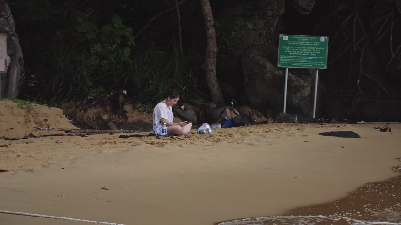 베트남 콩 다오 섬 의 모래 해변 에 앉아 킨들 책 을 읽고 있는 여자