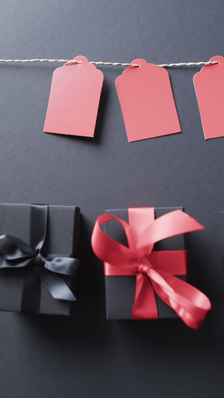Vertical video of gift tags on string, gift boxes with ribbons and copy space on black background