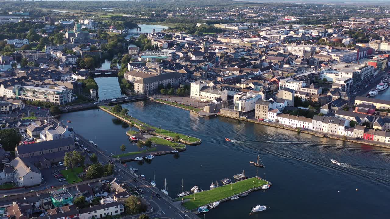 An overhead shot from a drone showcasing the skyline of the Irish city of Galway. A beautiful city with River Corrib
going down the middle, and the vast green countryside behind it.