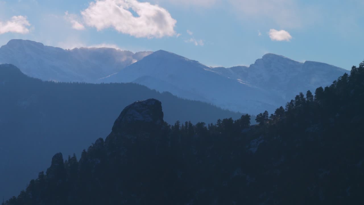 Veduta aerea con drone di Kruger Rock e Longs Peak, Estes Park, Colorado, al tramonto pomeridiano nel Parco Nazionale delle Montagne Rocciose. Paesaggio ventoso con neve fresca, cielo blu e nuvole, con la catena Front Range di Denver e una vetta prominente a sinistra.
