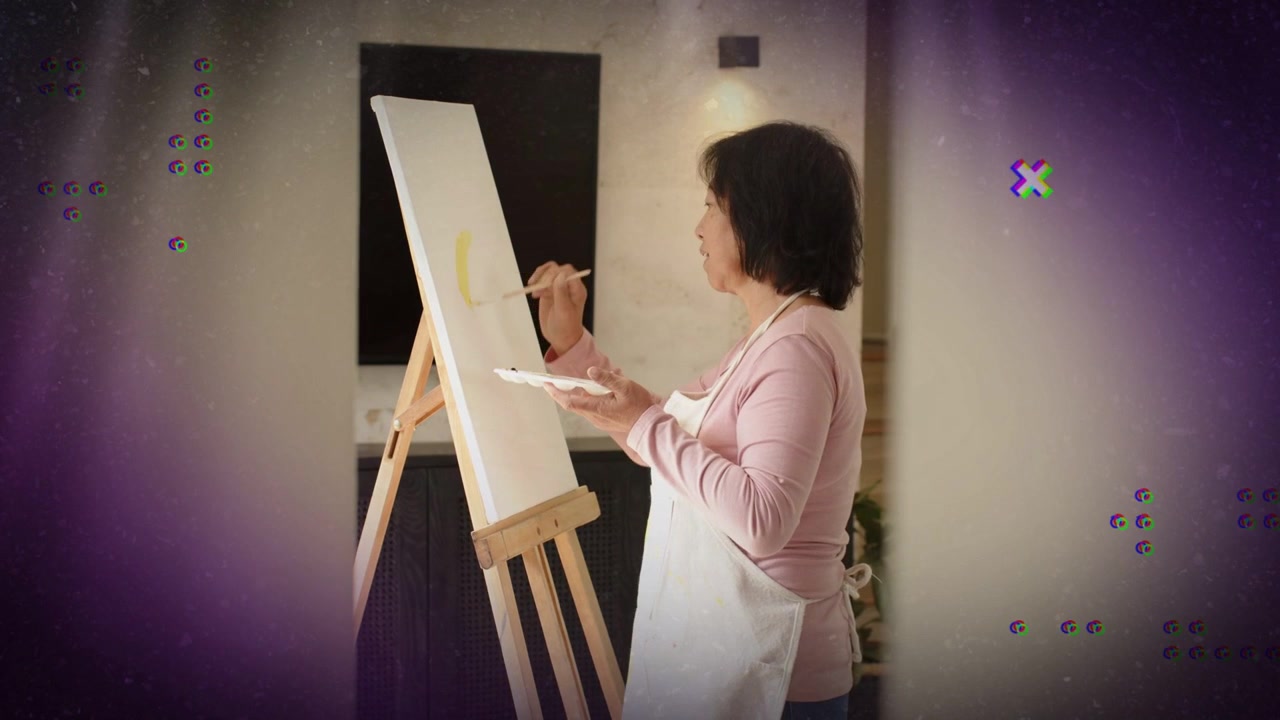 Artista sênior em pé no cavalete mergulhando pincel para formar arco amarelo enquanto sobreposição roxa aparece.