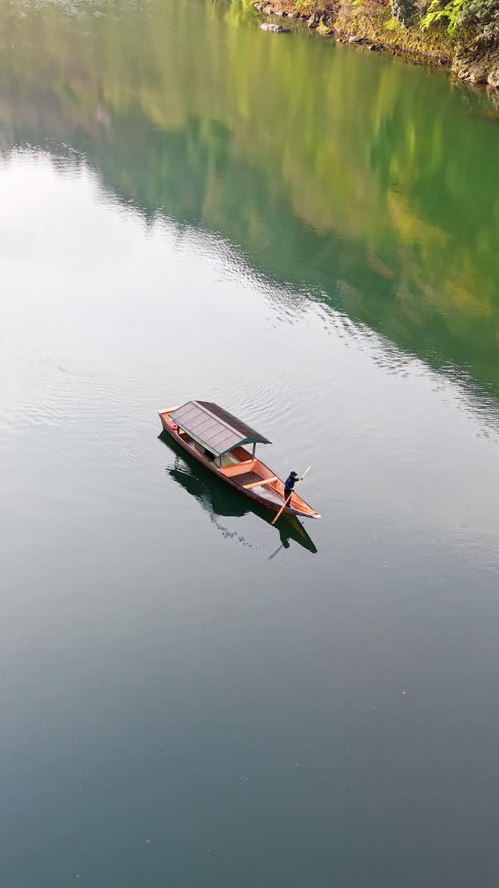 Aerial drone view of a boat moving on the Katsura River in Arashiyama, Japan in daylight