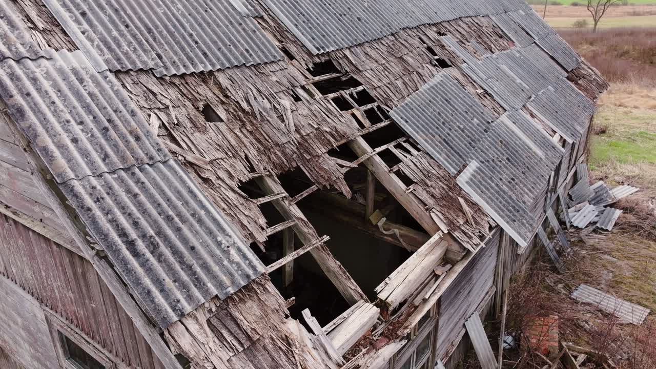 Weathered wooden barn, broken roof boards and gray metal sheets in spring light