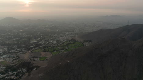 Toma-Aérea-Del-Carro-Sobre-El-Distrito-De-La-Molina-En-Lima-Perú,-Centrándose-En-El-Cementerio-Situado-Entre-Dos-Montañas