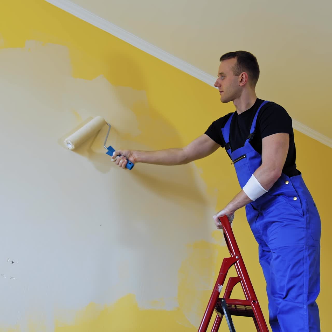 Worker repainting walls of the apartment from the ladder. Young builder male decorating walls into a new light color. Home repair