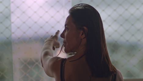 mujer morena de mediana edad señalando fuera de la ventana de su apartamento y luego mirando hacia la cámara, cámara lenta