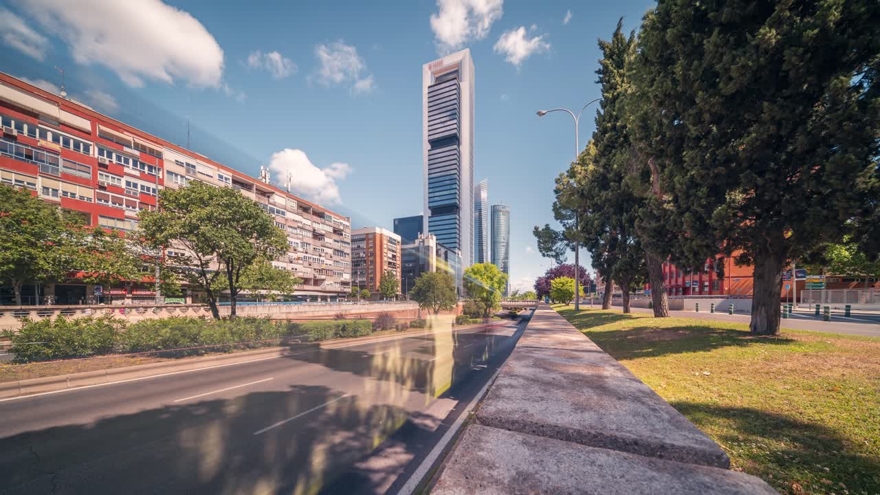 ultra gran ángulo timelapse de los rascacielos de madrid contra el cielo azul con nubes blancas en una soleada mañana de primavera de negocios y primer plano de automóviles que pasan