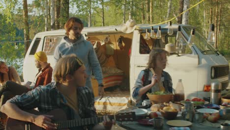 company of friends preparing food and playing guitar at campsite