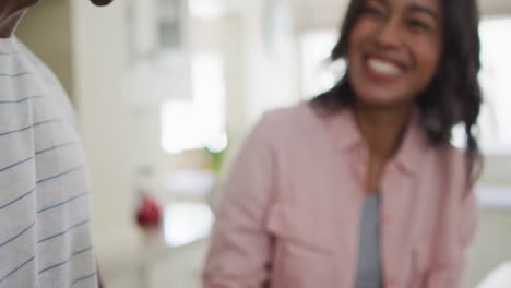 Close-up-of-happy-biracial-couple-in-kitchen-preparing-smoothie-together