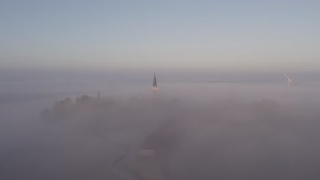 low morning fog at cornwerd with church sticking out of the clouds, aerial