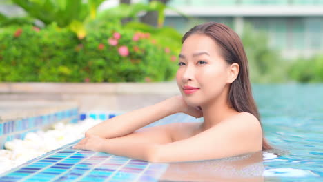 수영장에 있는 매력적인 젊은 여성이 호화로운 리조트 수영장 가장자리를 따라 몸을 기댄다