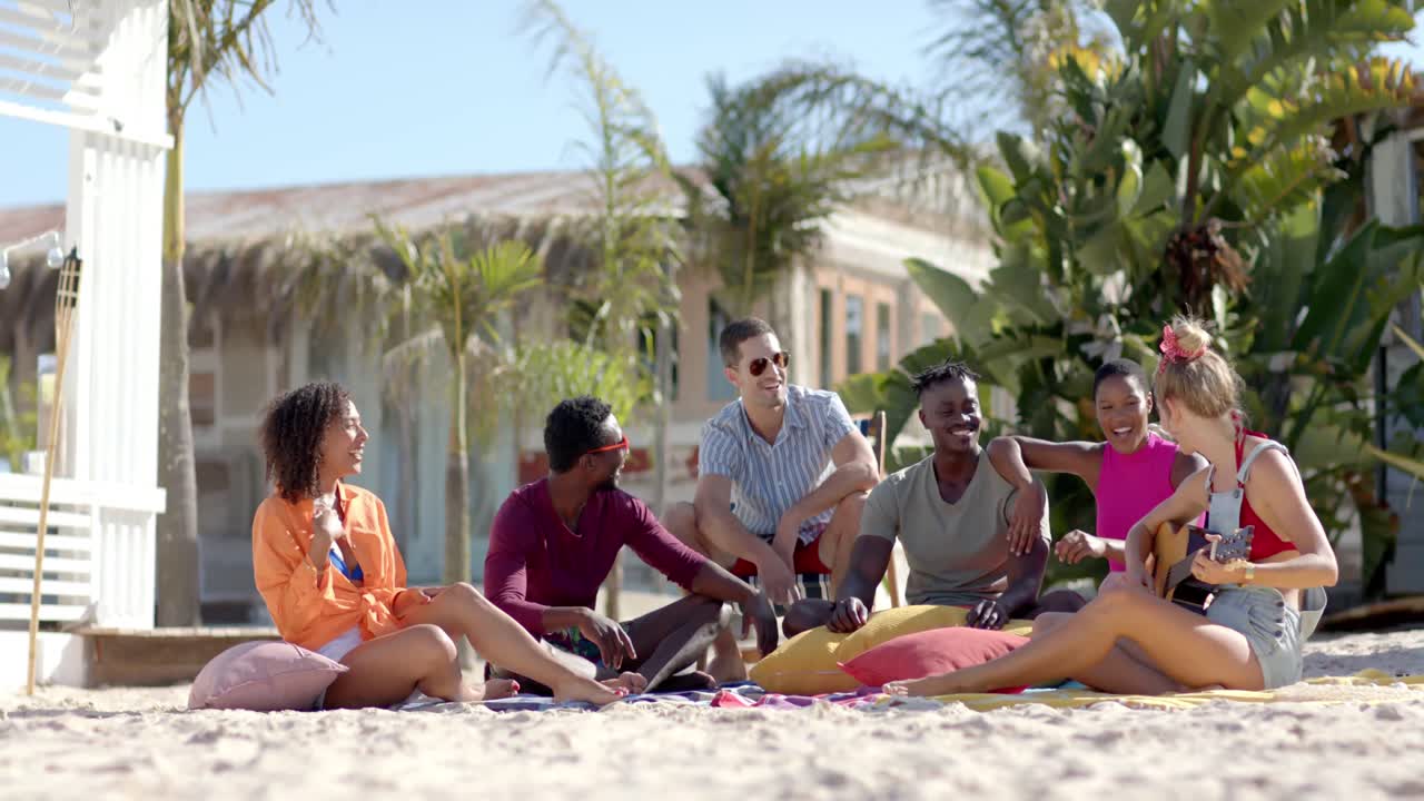 ⁇ 나무 와 해변집 이 있는 해변 에서 기타 를 연주 하고 앉아 있는 행복 한 다양한 친구 들