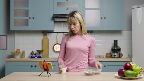 woman eating a snack while having a video call in her kitchen.