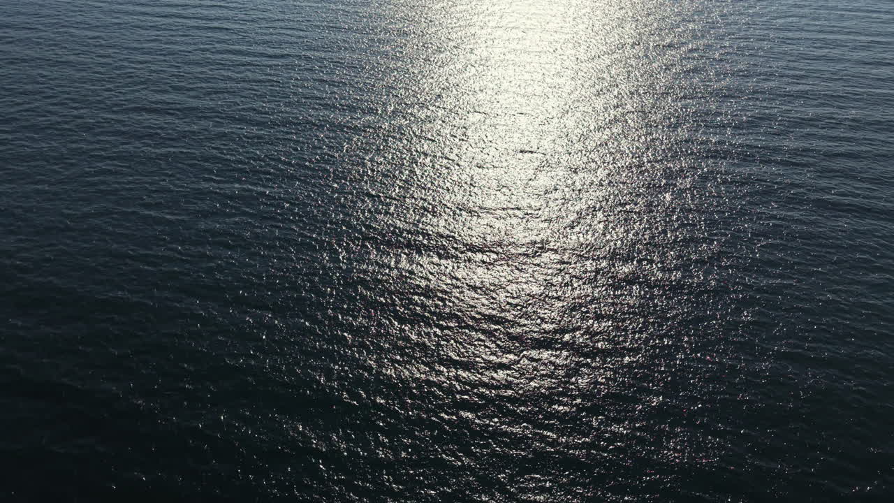 Sunlight reflecting on ocean water in the early afternoon creates a shimmering effect on the surface near the coastline
