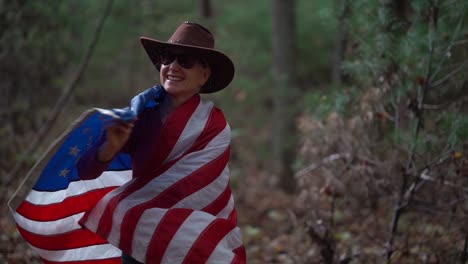 woman in sunglasses and cowboy hat wraps us flag around her and gives a yes sign with her head