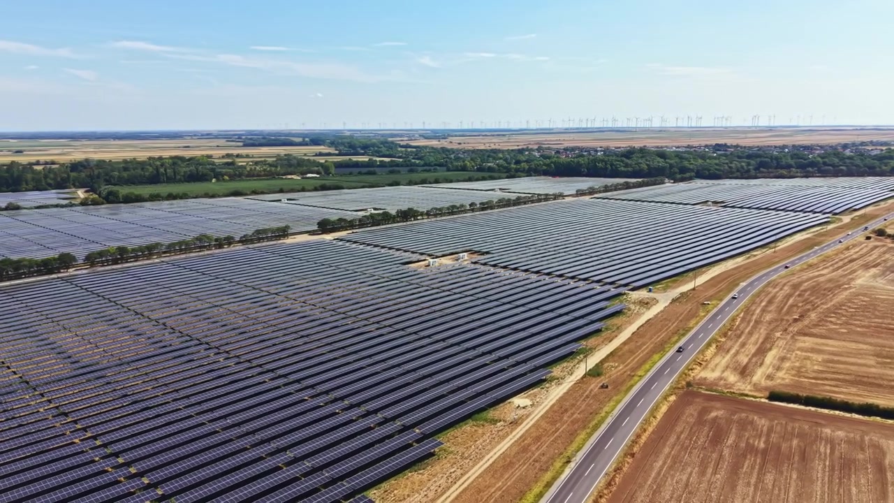 Solpaneler dækker et stort markområde i et landdistrikt og genererer vedvarende energi under en klar blå himmel om eftermiddagen.