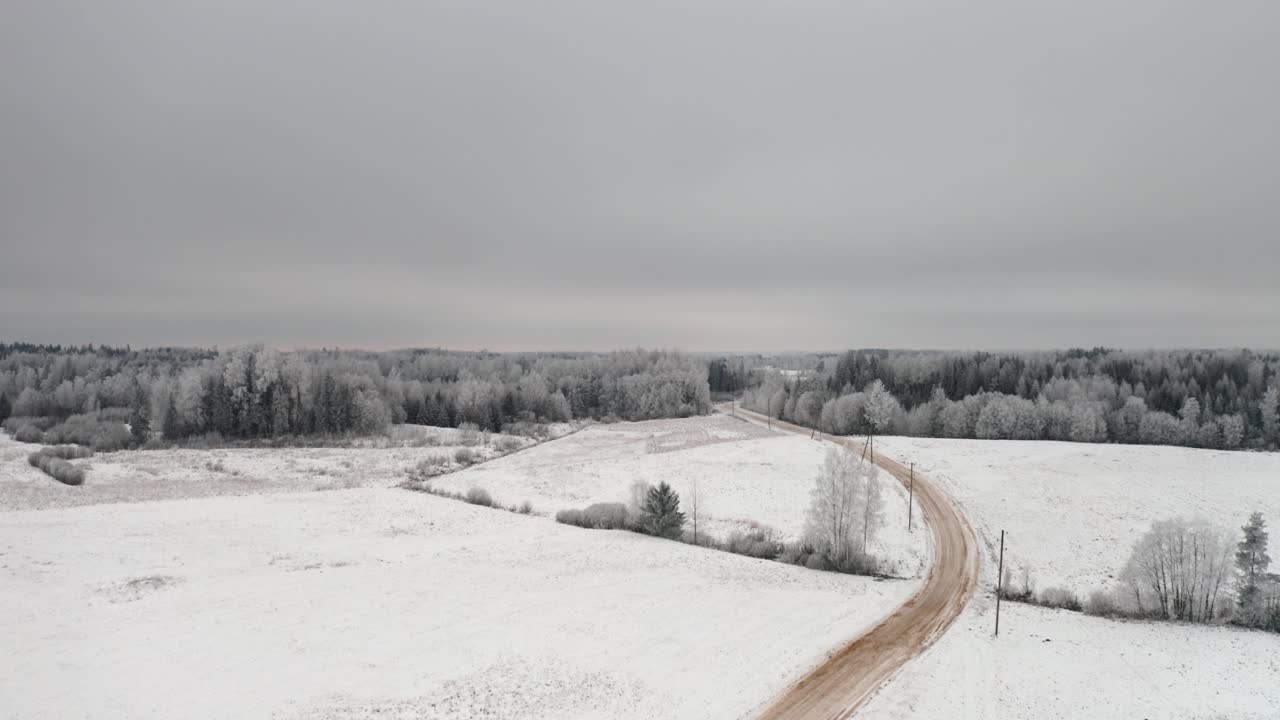 Winter magic from above with hoar frost and snow blanket over the landmark. Aerial drone shot over a gravel road in countryside and frozen forest in the background.