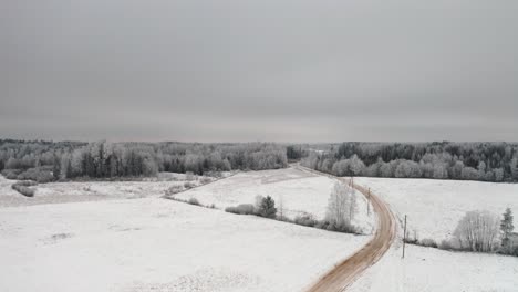 winter magic from above with hoar frost and snow blanket over the landmark. aerial drone shot over a gravel road in countryside and frozen forest in the background.