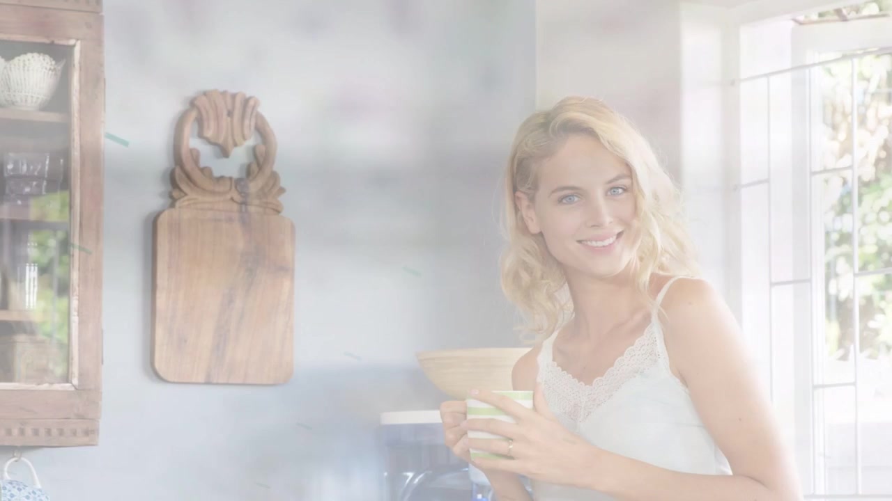 Donna che entra in una cucina luminosa e sorseggia da una tazza vicino alla finestra, con vapore animato, per la salute.