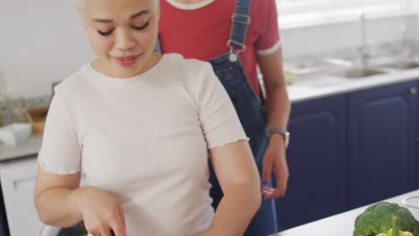 Happy-diverse-female-couple-cooking-vegetables-and-embracing-in-kitchen