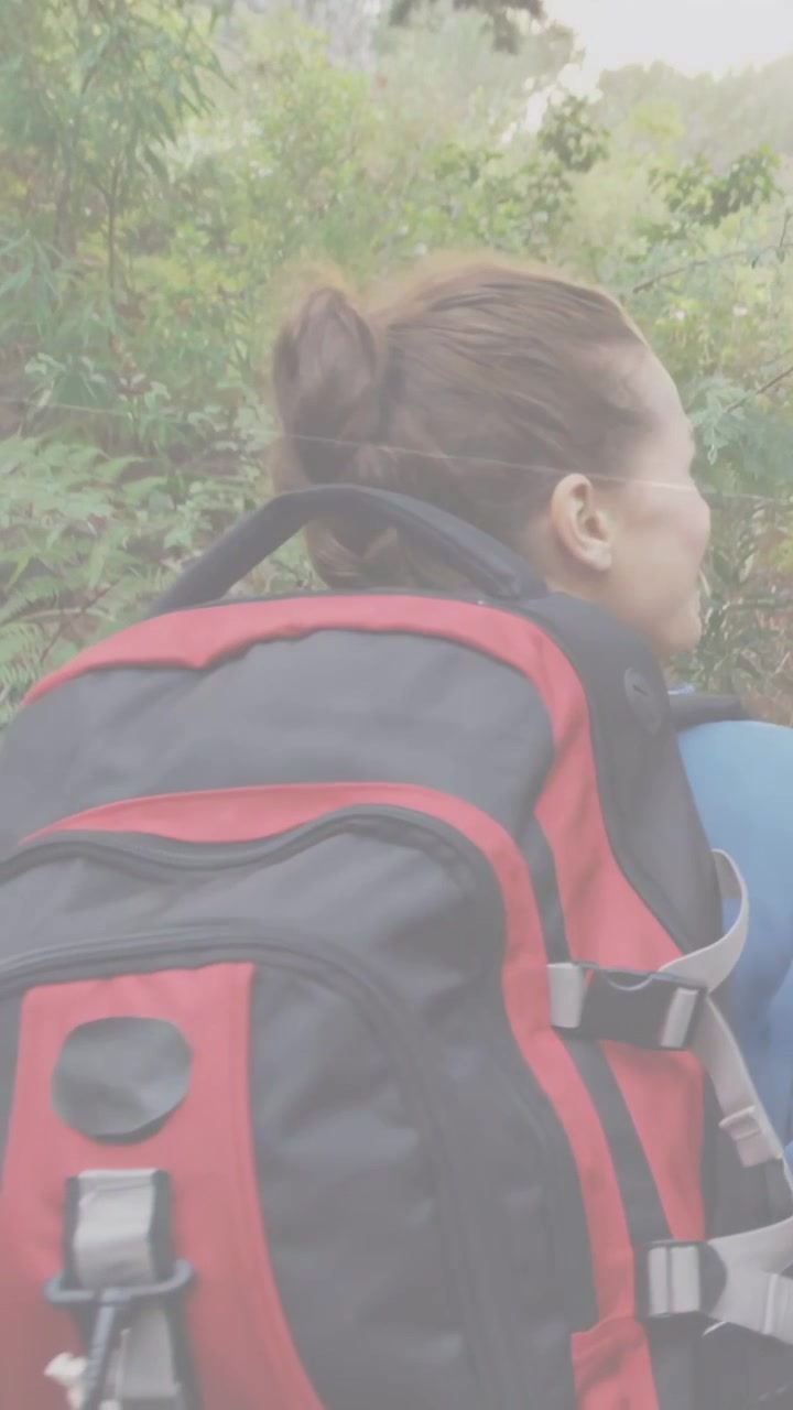 Video verticale: Donna con uno zaino rosso su un sentiero escursionistico che ammira il panorama, girandosi mentre il partner la segue.