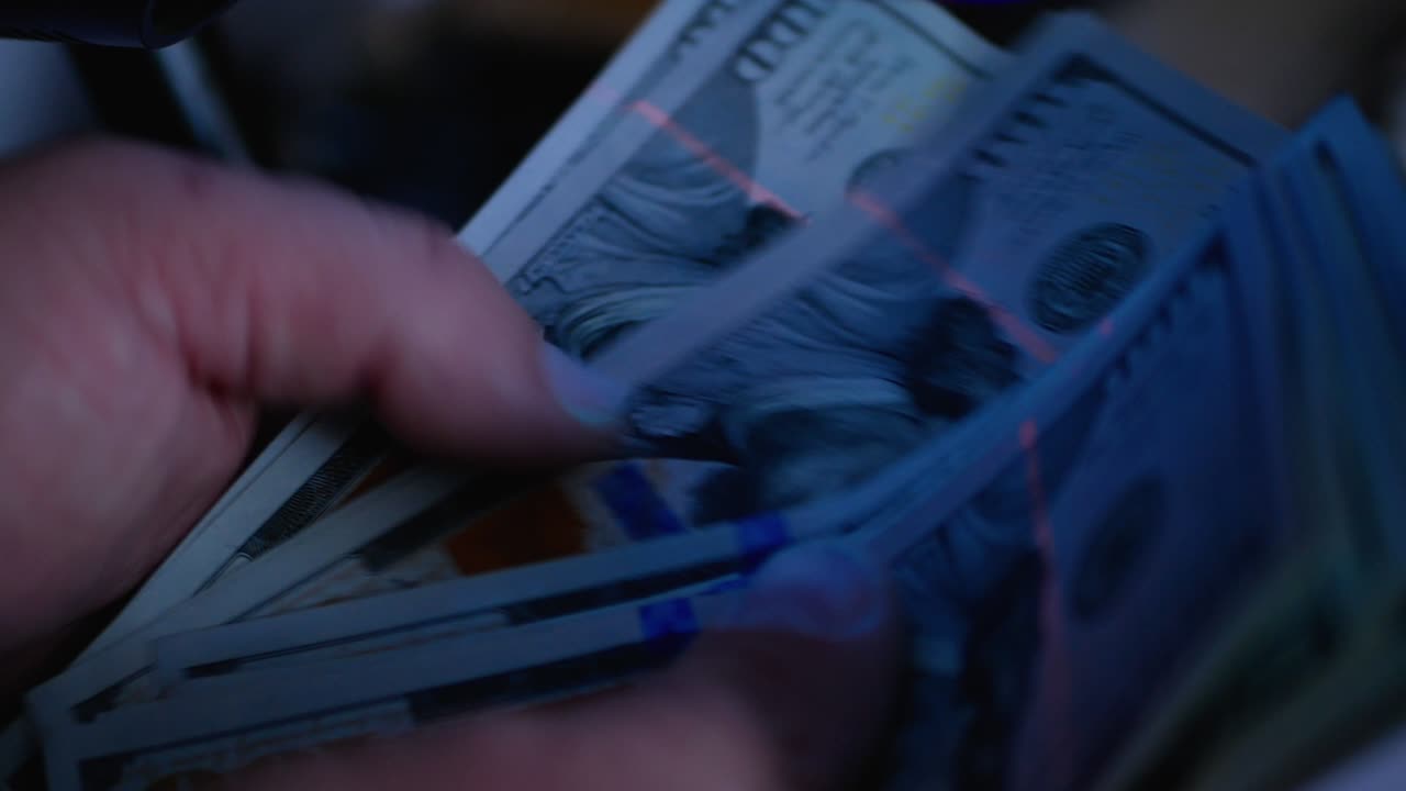 Examining one hundred dollar banknotes with a money detector. Detector banknotes.