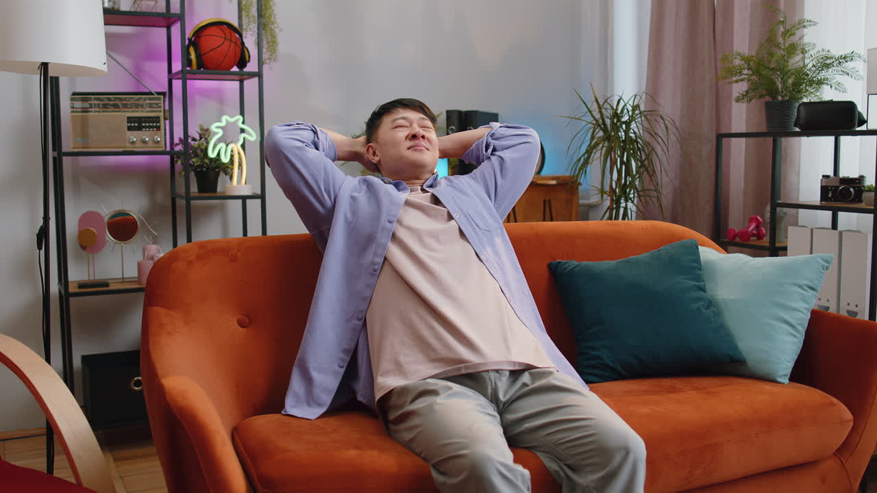 Tired asian man enjoy relaxing on home sofa resting napping after hard working day closed his eyes