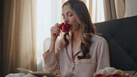 Woman reading and enjoying coffee and a croissant in bed