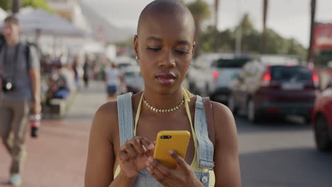 portrait of happy african american woman using smartphone enjoying texting sending sms messages sharing vacation experience in sunny urban street