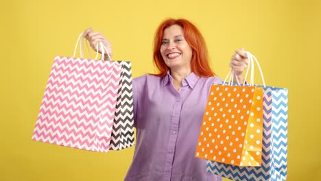 happy red-haired woman holding shopping bags on yellow background