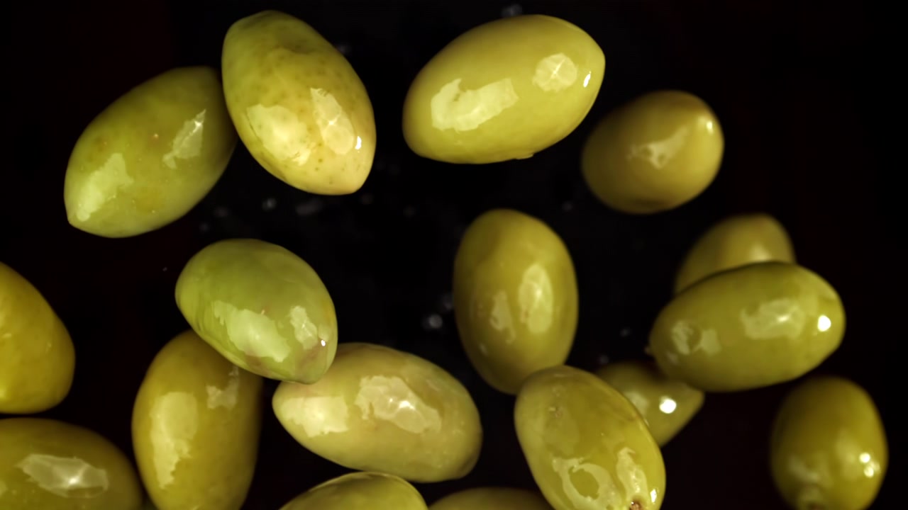 Olive verdi che cadono in super slow motion su sfondo nero.