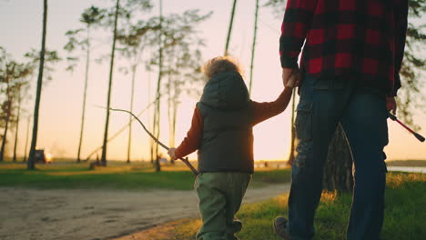 cute little child is holding hand of grandfather or dad walking together to fishing in sunset time