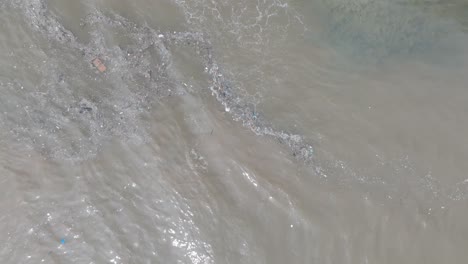 Top-down-aerial-drone-shot-over-polluted-sewage-water-and-floating-trash-with-debris-over-dead-coral-reef-mixing-with-turquoise-water-and-tropical-coastine-in-Bali-Indonesia