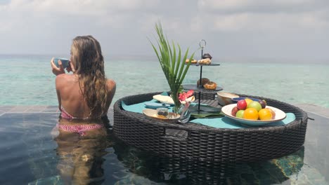 slow motion: beautiful young woman eats breakfast in her private pool from floating tray.